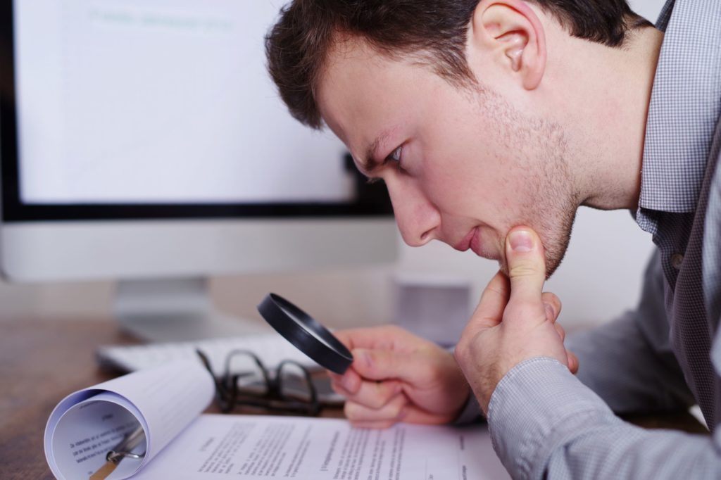 man reviewing document with magnifying glass